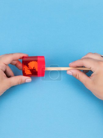 Téléchargez les photos : Gros plan d'une jeune femme affûtant un crayon d'ardoise d'entraînement dans un aiguiseur en plastique rouge sur fond bleu - en image libre de droit