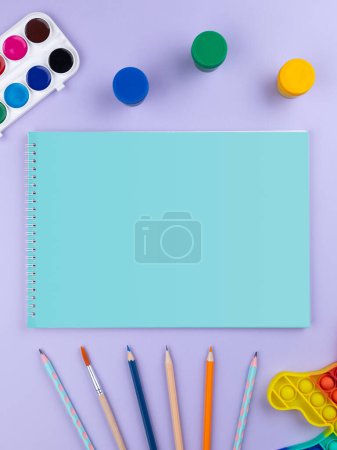 Foto de Cuaderno de bocetos con varios artículos de papelería sobre un fondo multicolor brillante, espacio de copia - Imagen libre de derechos