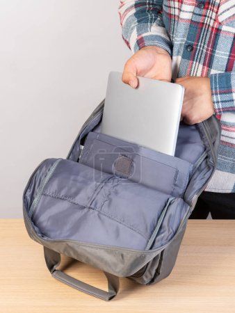 Téléchargez les photos : Un homme emballe son ordinateur portable dans un sac à dos, gros plan - en image libre de droit