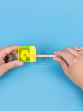 Téléchargez les photos : Gros plan d'une jeune femme affûtant un crayon d'ardoise d'entraînement dans un taille-crayon jaune sur fond bleu - en image libre de droit