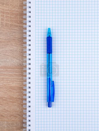 Foto de Una pluma azul yace en un cuaderno sobre una mesa de madera. El bolígrafo está listo - Imagen libre de derechos