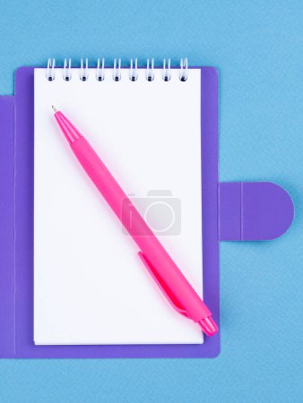 Foto de El primer plano del cuaderno, un bolígrafo rosa sobre una mesa azul están listos para la lección. Papelería. Regreso a la escuela - Imagen libre de derechos