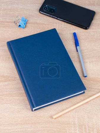 Téléchargez les photos : Gros plan sur le carnet bleu, un stylo bleu, téléphone sur une table en bois sont prêts pour la leçon. Papeterie. Retour à l'école - en image libre de droit
