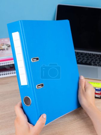 Téléchargez les photos : Gros plan des mains d'une femme tenant des documents dans une manche dans un dossier bleu assis à la maison sur la table - en image libre de droit