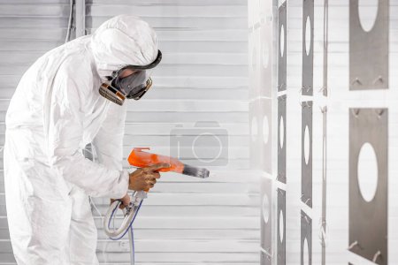 Photo for A decorator, painter in protective overalls paints parts with a spray gun indoors. Man painting metal products with a spray gun - Royalty Free Image
