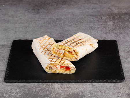 Foto de Shawarma roll en lavash con palitos de cangrejo, verduras frescas, salsa crema y papas fritas sobre un fondo de madera. Enfoque selectivo - Imagen libre de derechos