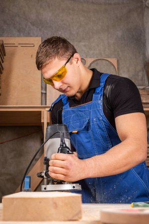 Téléchargez les photos : Menuisier masculin utilisant une ponceuse électrique pour polir la planche de bois dans un atelier de menuiserie - en image libre de droit