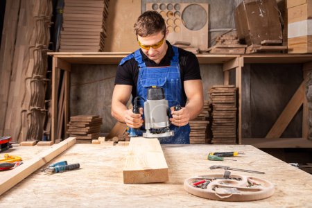 Foto de Joven por profesión carpintero constructor equivale a una fresadora de madera en una mesa de madera en el taller - Imagen libre de derechos