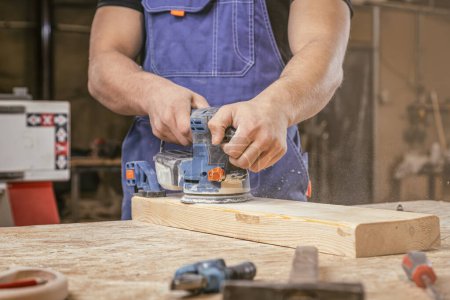 Foto de Joven carpintero moliendo madera con papel de lija en carpintería o taller de bricolaje. Lijadora eléctrica trabajando en carpintería - Imagen libre de derechos