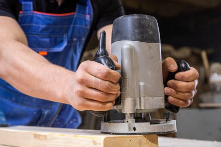 Photo for Young man by profession carpenter builder equals a wooden milling machine on a wooden table in the workshop - Royalty Free Image
