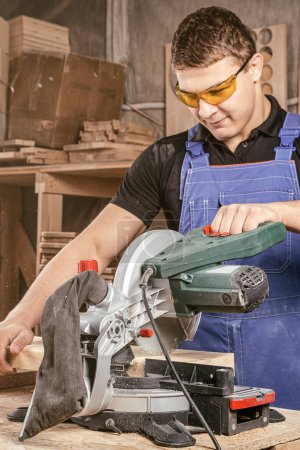 Photo for Young man builder carpenter sawing board with circular saw in workshop - Royalty Free Image
