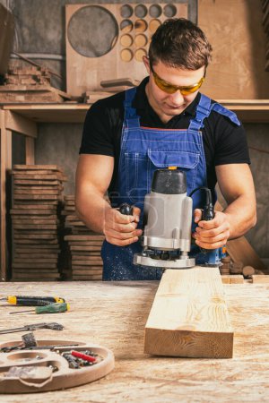 Photo for Male carpenter using electric sander to polish wooden plank in joinery workshop - Royalty Free Image