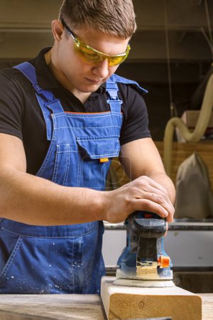 Foto de Retrato de un carpintero joven usando una máquina de lijar eléctrica para pulir un taller de peluquería de madera - Imagen libre de derechos