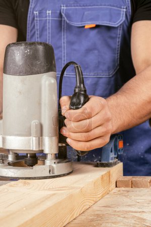 Foto de Un fuerte carpintero masculino con ropa de trabajo trabaja con entusiasmo y sierra una tabla de madera sobre una mesa de madera en un taller industrial - Imagen libre de derechos