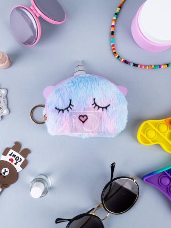 Photo for On the table is a children's fur multi-colored wallet in the shape of a unicorn with a horn and ears with other children's things on the table - Royalty Free Image