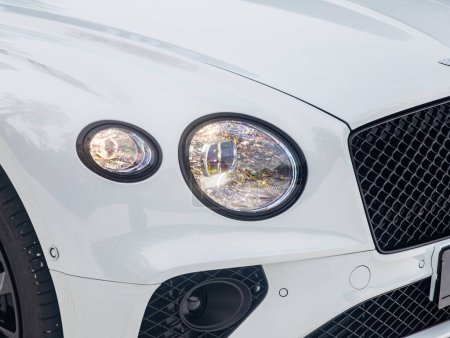 Téléchargez les photos : Novossibirsk, Russie - 05 janvier 2024 : blanc Bentley Continental GT, Phare d'une voiture de luxe moderne gros plan. Phare de voiture en verre brillant avec éblouissement de la lumière - en image libre de droit