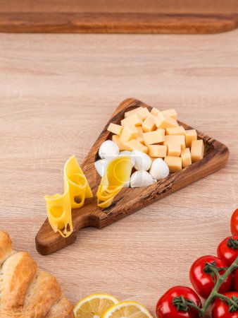 Assorted cheese and vegetables - served on a wooden board with tomatoes and bread