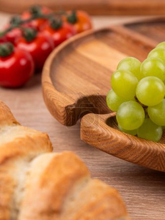 Photo for Close-up of a wooden oak plate with vegetables and bread in the background - Royalty Free Image
