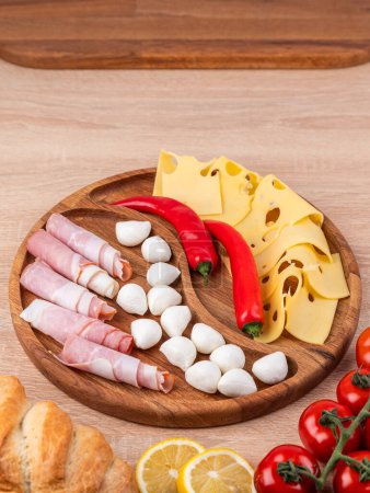 Photo for Top view of a round wooden plate with different snacks: sausages, cheese, peppers, standing on a wooden table. - Royalty Free Image