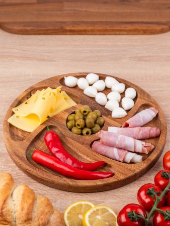 Photo for Top view of a round wooden plate with different snacks: sausages, cheese, peppers, standing on a wooden table. - Royalty Free Image