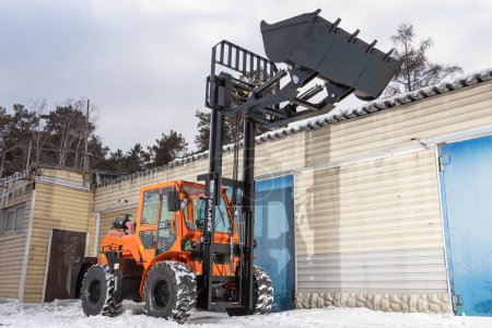Foto de Novosibirsk, Rusia - 29 de febrero de 2024: Tractor naranja, cargador contra garaje - Imagen libre de derechos