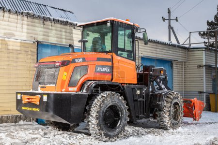 Foto de Novosibirsk, Rusia - 29 de febrero de 2024: Tractor naranja, cargador contra garaje - Imagen libre de derechos