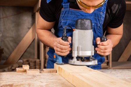 Téléchargez les photos : Menuisier masculin utilisant une ponceuse électrique pour polir la planche de bois dans un atelier de menuiserie - en image libre de droit
