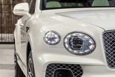 Téléchargez les photos : Novossibirsk, Russie - 01 mai 2024 : blanc Bentley Bentayga, Phare d'une voiture de luxe moderne gros plan. Phare de voiture en verre brillant avec éblouissement de la lumière - en image libre de droit