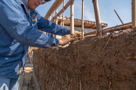 Foto de A man building a wall with reed and mud, bioconstruction - Imagen libre de derechos