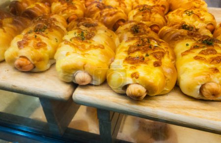 Téléchargez les photos : Gros plan pain à la saucisse sur l'étagère avec de la lumière chaude dans la boulangerie. - en image libre de droit