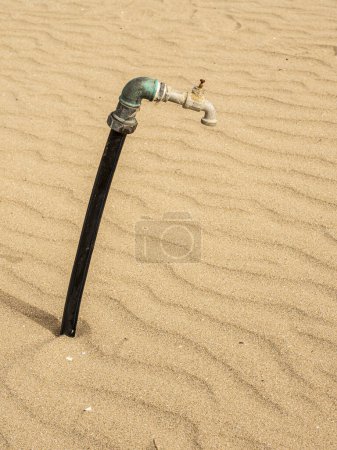 Wasserleitung in den Sand. Verlassener Wasserhahn: Symbol für Wasserkrise und Umweltzerstörung