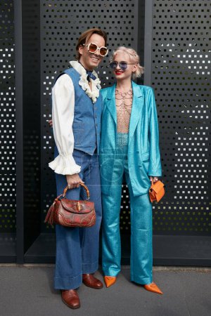 Téléchargez les photos : MILAN, ITALIE - 23 SEPTEMBRE 2022 : Homme et femme avec pantalon en denim et sac Gucci et costume métallique turquoise avant le défilé Gucci, Milan Fashion Week street style - en image libre de droit