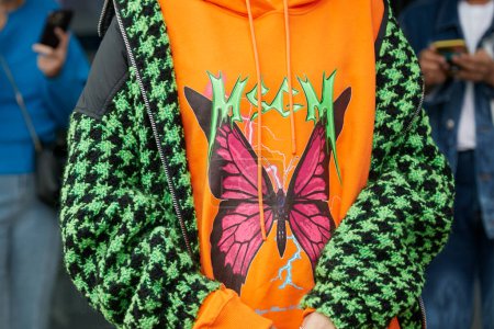 Foto de MILÁN, ITALIA - 24 DE SEPTIEMBRE DE 2022: Mujer con sudadera con capucha MSGM naranja con mariposa y houndstooth chaqueta negra y verde antes del desfile de moda MSGM, Milan Fashion Week street style - Imagen libre de derechos