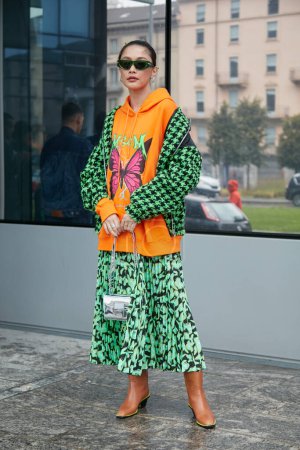 Téléchargez les photos : MILAN, ITALIE - 24 SEPTEMBRE 2022 : Femme avec sweat à capuche orange MSGM avec veste papillon et pied-de-poule noire et verte avant le défilé MSGM, Milan Fashion Week street style - en image libre de droit