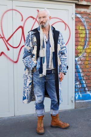 Foto de MILAN, ITALY - JANUARY 14, 2023: Man with blue denim trousers, white and blue scarf and glasses before Fendi fashion show, Milan Fashion Week street style - Imagen libre de derechos