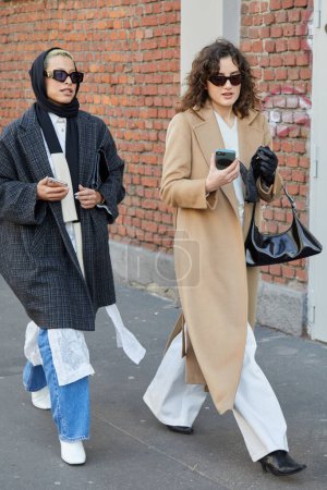 Téléchargez les photos : MILAN, ITALY - JANUARY 14, 2023: Women with sunglasses and gray and beige coat before Fendi fashion show, Milan Fashion Week street style - en image libre de droit