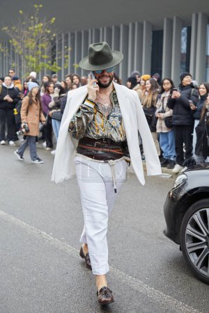 Téléchargez les photos : MILAN, ITALY - JANUARY 15, 2023: Man with white jacket and trousers and olive green hat before Etro fashion show, Milan Fashion Week street style - en image libre de droit