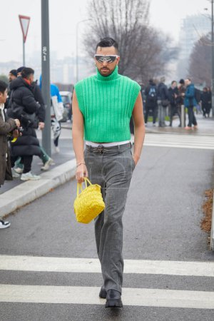 Foto de MILAN, ITALY - JANUARY 15, 2023: Man with green turtleneck, gray trousers and yellow bag before Prada fashion show, Milan Fashion Week street style - Imagen libre de derechos