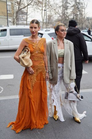 Foto de MILÁN, ITALIA - 22 DE FEBRERO DE 2023: Mujeres con vestido naranja y falda de encaje blanco y chaqueta beige antes del desfile de moda Alberta Ferretti, Milan Fashion Week street style - Imagen libre de derechos