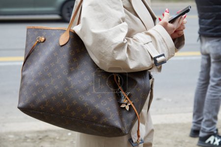 Téléchargez les photos : MILAN, ITALIE - 22 FÉVRIER 2023 : Femme avec un sac Louis Vuitton marron et un trench coat beige avant le défilé Fendi, Milan Fashion Week street style - en image libre de droit