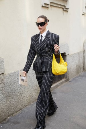 Téléchargez les photos : MILAN, ITALIE - 23 FÉVRIER 2023 : Femme avec veste et pantalon à rayures et sac en cuir jaune avant le défilé Genny, Milan Fashion Week street style - en image libre de droit