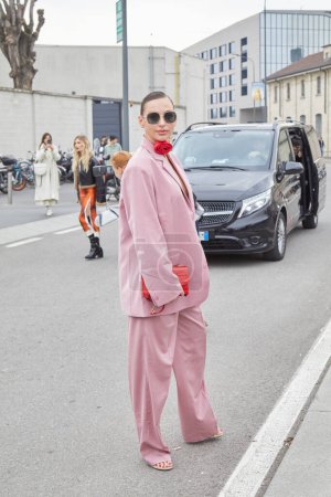 Foto de MILÁN, ITALIA - 23 DE FEBRERO DE 2023: Mujer con chaqueta rosa y pantalones y collar de flores rojas antes del desfile de moda Prada, Milan Fashion Week street style - Imagen libre de derechos