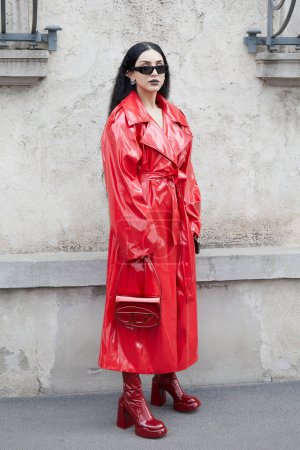 Foto de MILÁN, ITALIA - 23 DE FEBRERO DE 2023: Mujer con impermeable rojo y bolsa Diesel antes del desfile de moda Prada, Milan Fashion Week street style - Imagen libre de derechos