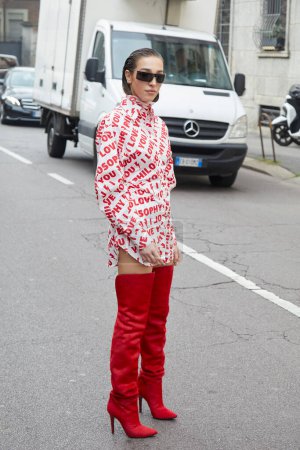 Téléchargez les photos : MILAN, ITALIE - 24 FÉVRIER 2023 : Ginevra Mavilla avec robe blanche aux écritures rouges et bottes rouges avant Philosophie par Lorenzo Serafini défilé de mode, Milan Fashion Week street style - en image libre de droit