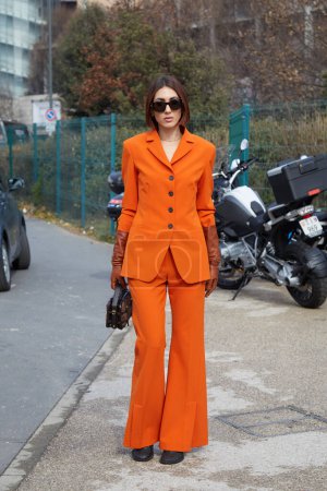 Foto de MILÁN, ITALIA - 25 DE FEBRERO DE 2023: Ludovica Ragazzo con chaqueta naranja, pantalones y guantes de cuero marrón antes del desfile de moda Ferragamo, Milan Fashion Week street style - Imagen libre de derechos