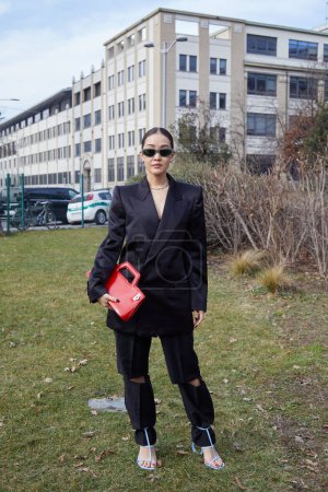 Téléchargez les photos : MILAN, ITALIE - 25 FÉVRIER 2023 : Femme avec veste noire, pantalon et sac en cuir rouge avant le défilé Ferragamo, Milan Fashion Week street style - en image libre de droit