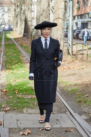 Foto de MILÁN, ITALIA - 25 DE FEBRERO DE 2023: Mujer con sombrero y abrigo negro antes de Dolce y Gabbana desfile de moda, Milan Fashion Week street style - Imagen libre de derechos