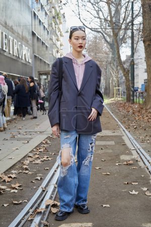 Téléchargez les photos : MILAN, ITALIE - 25 FÉVRIER 2023 : Femme avec veste grise, sweat à capuche rose et pantalon déchiré en denim bleu avant le défilé Dolce et Gabbana, Milan Fashion Week street style - en image libre de droit