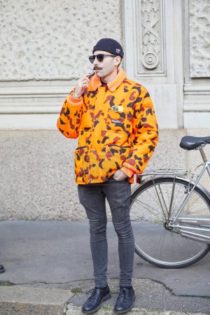 Téléchargez les photos : MILAN, ITALIE - 25 FÉVRIER 2023 : Homme avec veste rembourrée Refrigiwear orange et pantalon en denim gris avant le défilé Missoni, Milan Fashion Week street style - en image libre de droit