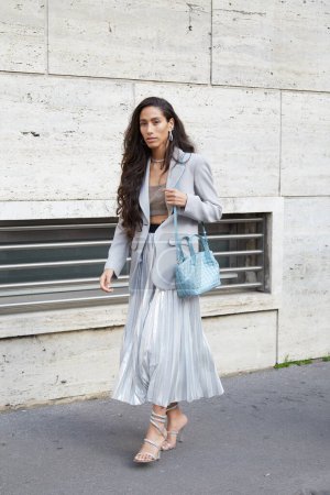 Téléchargez les photos : MILAN, ITALIE - 25 FÉVRIER 2023 : Femme avec sac bleu clair, jupe plissée argentée et veste grise avant le défilé Missoni, Milan Fashion Week street style - en image libre de droit